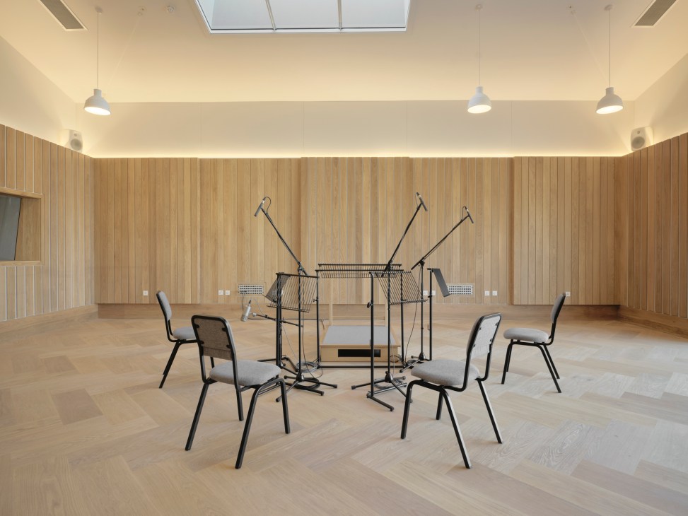 Recording studio microphones arranged in a circle with stands and acoustic panels on wooden flooring.