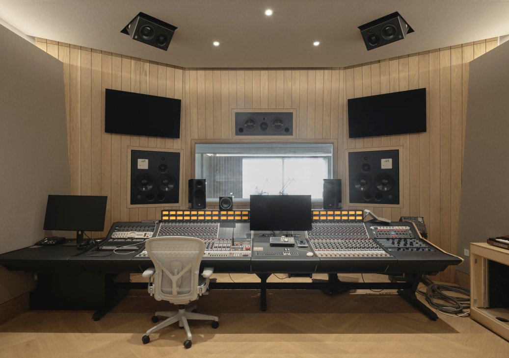 Professional mixing console and recording studio equipment with wooden wall paneling and acoustic speakers.
