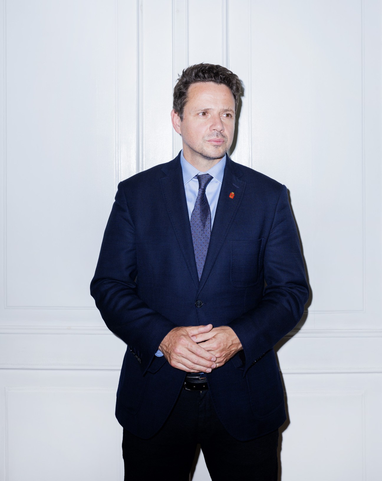 Warsaw Mayor Rafal Trzaskowski in a dark navy blazer and blue tie against a white paneled background.
