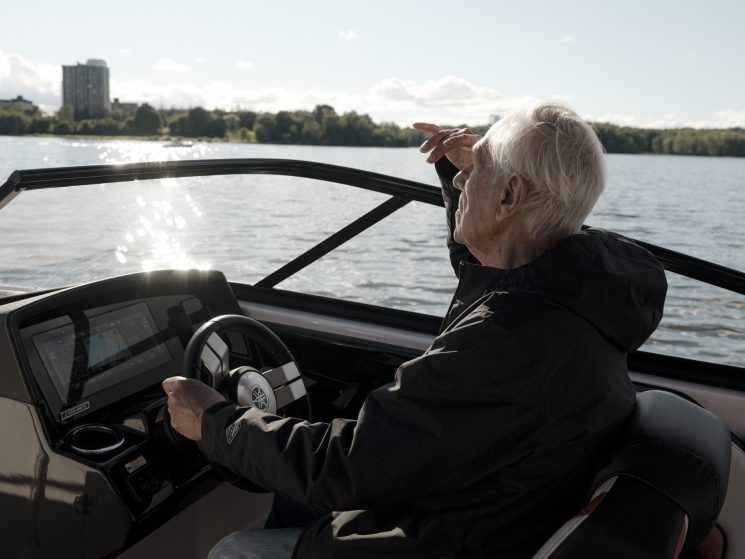 Douglas Cardinal navigating his boat on the Ottawa River with Parliament Hill visible in the background