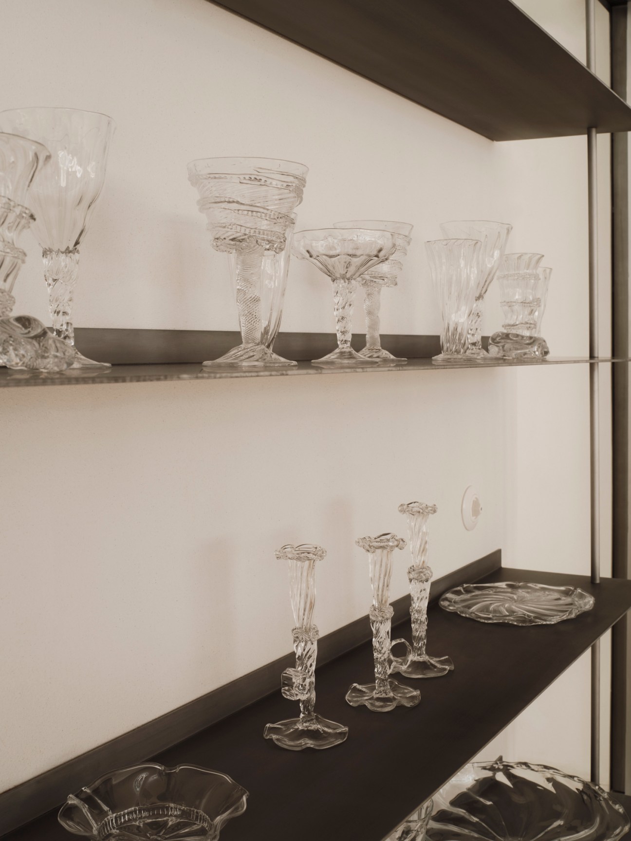 Collection of clear crystal glassware including goblets, bowls and stemware displayed on dark shelves
