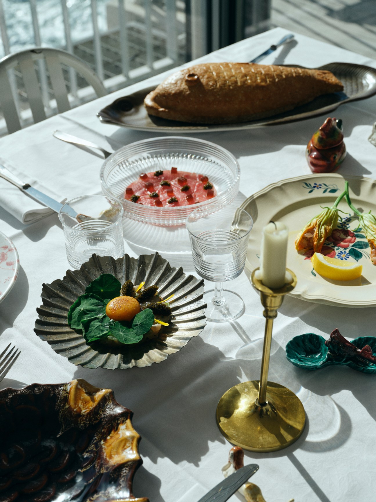 Elegant table setting with whole fish, raw fish dish, wine glass and candle at Tuba restaurant's chef's table