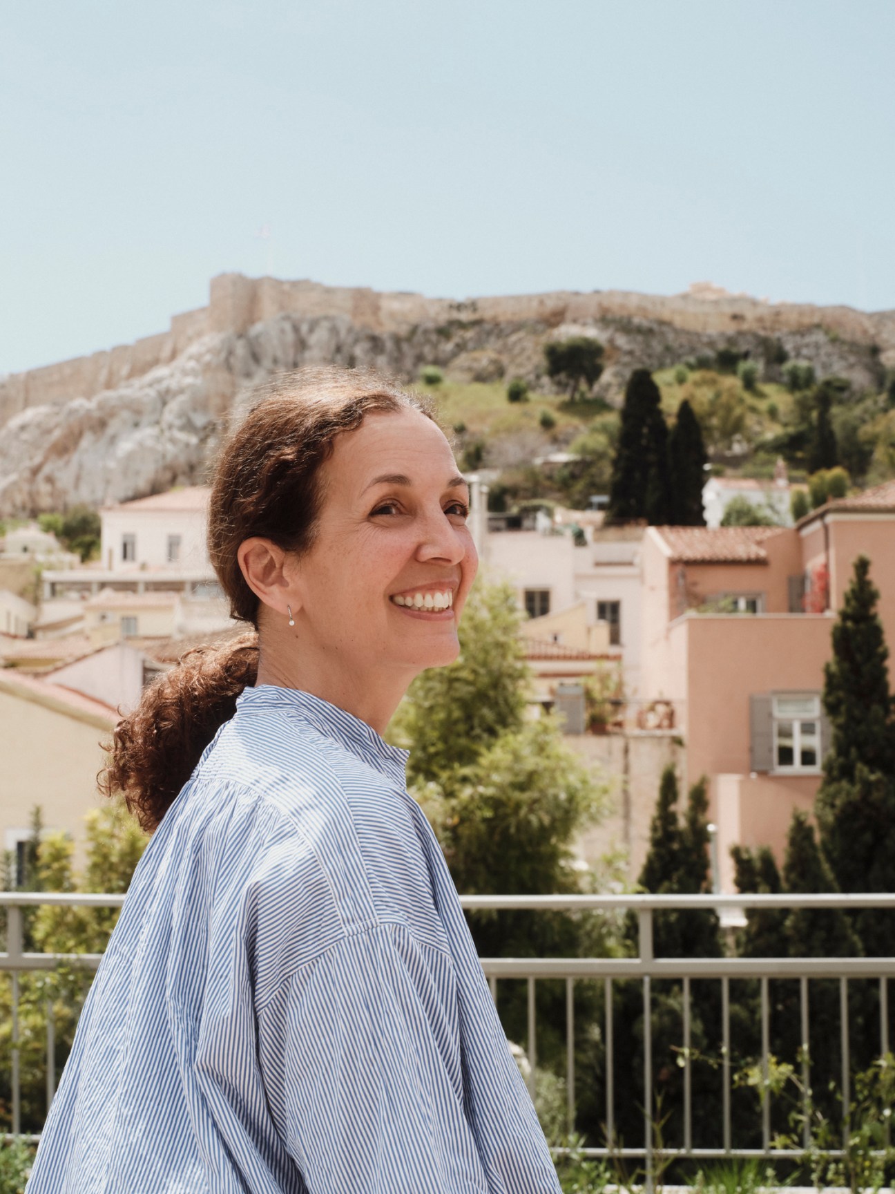 Maria Lemos smiling on a terrace overlooking Athens with the Acropolis visible in the background