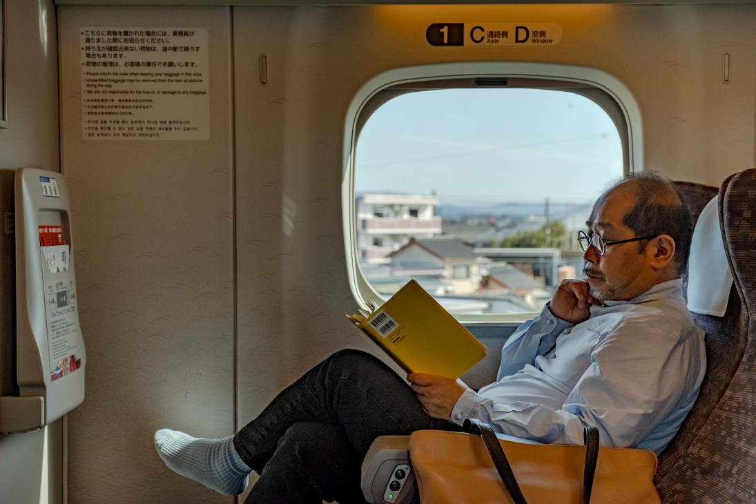Jun Aoki reading a yellow book while seated in first class on the Shinkansen bullet train