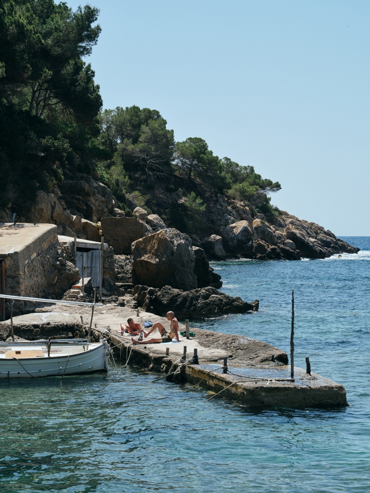 Rocky coastline with stone pier extending into clear blue Mediterranean waters with small boat moored nearby