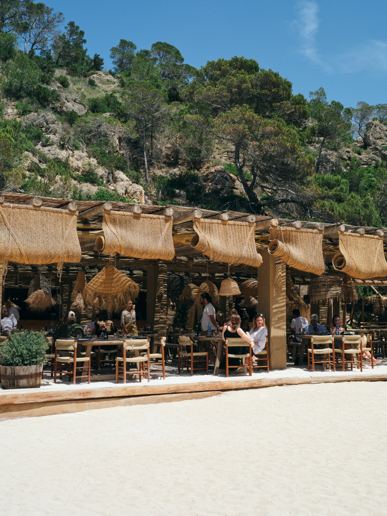 Rustic beachside restaurant terrace with woven reed sun shades and wooden dining tables