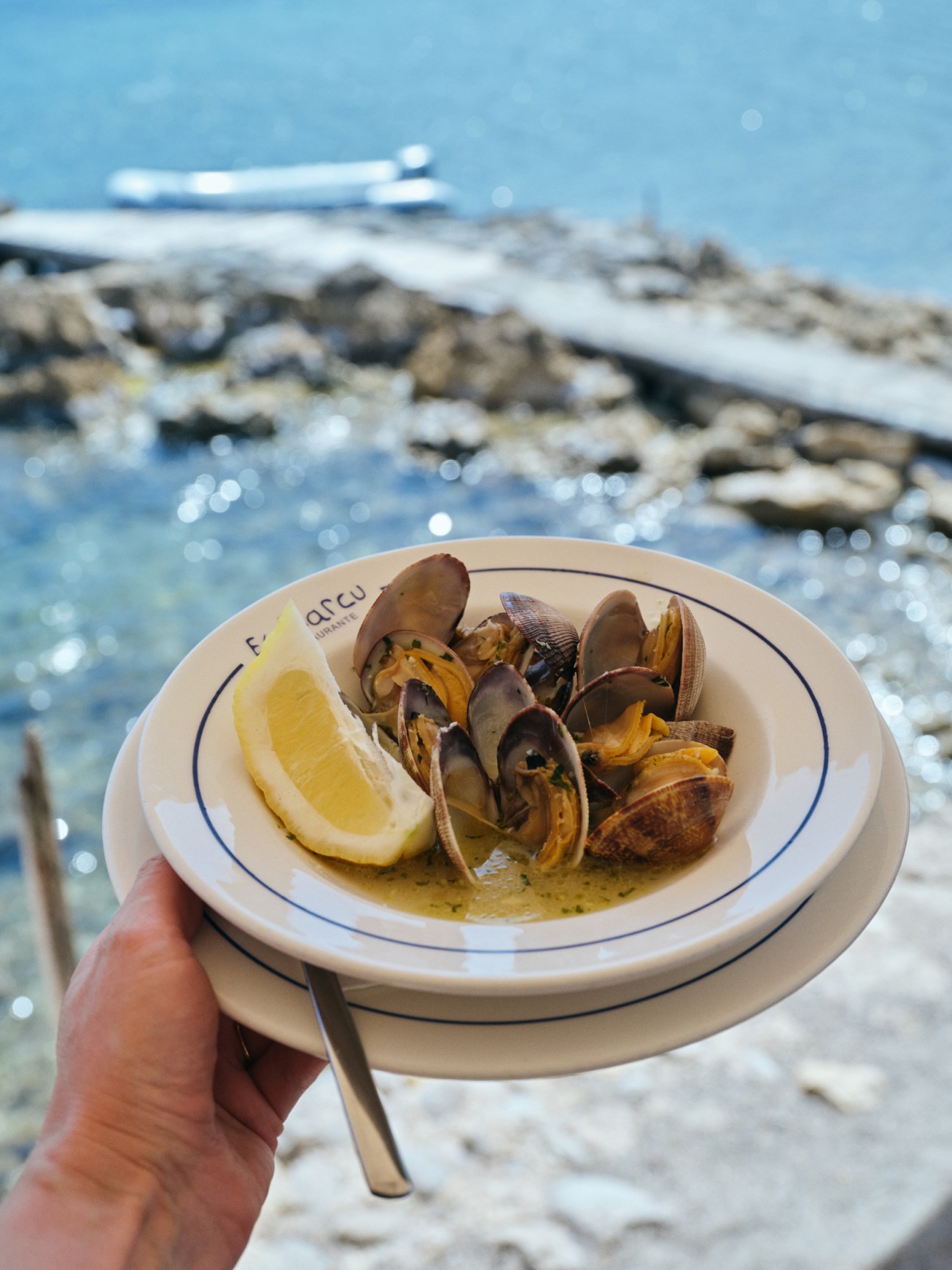 Clams served in white bowl with lemon wedge and broth at seaside restaurant