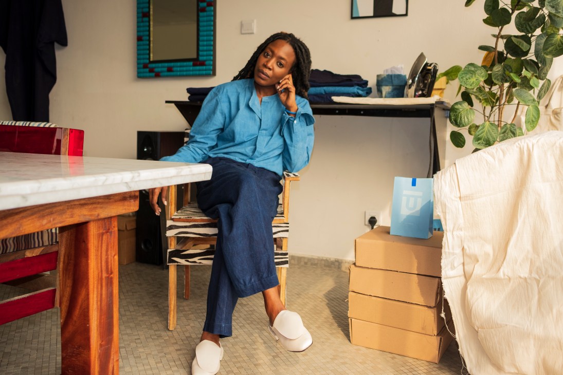Woman in blue shirt and jeans sitting at table with phone, packages stacked nearby in modern interior