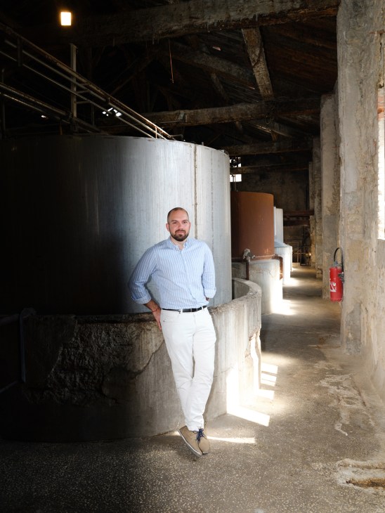 Raphael Seghin stands in an industrial space with large metal tanks and concrete walls.