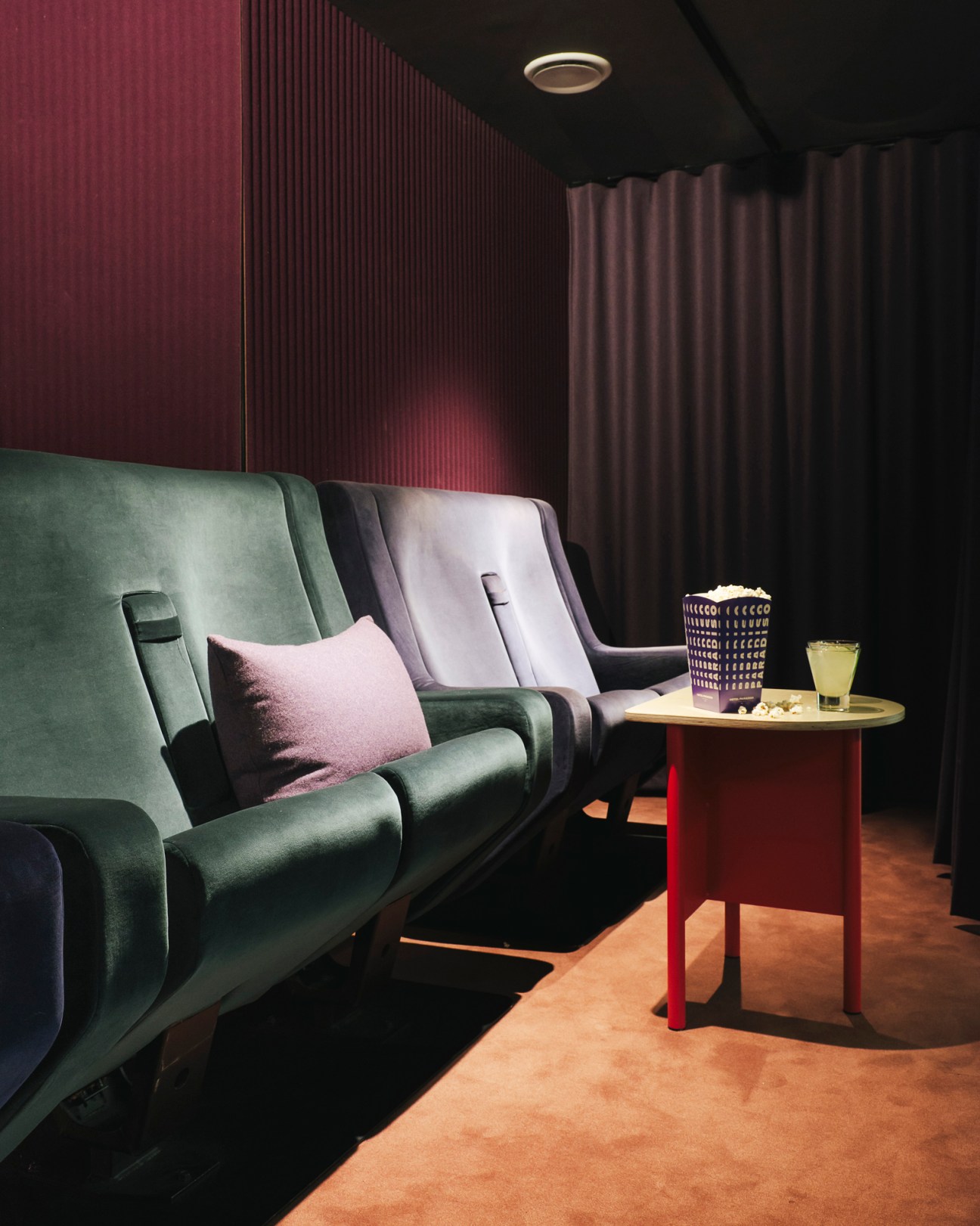 Modern lounge seating with green and lavender armchairs and pink cushion in a private cinema box at Hotel Paradiso Paris.