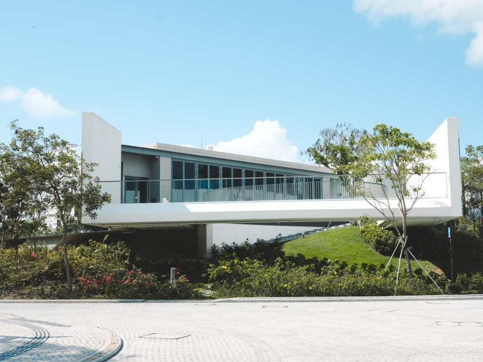 Modern white building with glass facades and balcony elevated on pillars in landscaped park setting