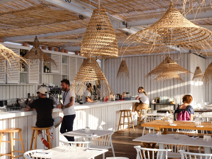 The Babel Community's rooftop terrace with woven pendant lights, white chairs, and people at the bar counter.