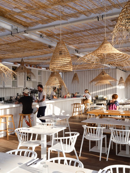 The Babel Community's rooftop terrace with woven pendant lights, white chairs, and people at the bar counter.