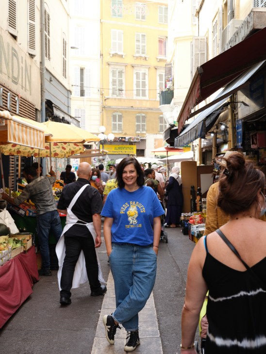 Film-maker and writer Vérane Frediani walks through a bustling Marseille market street lined with vendor stalls.