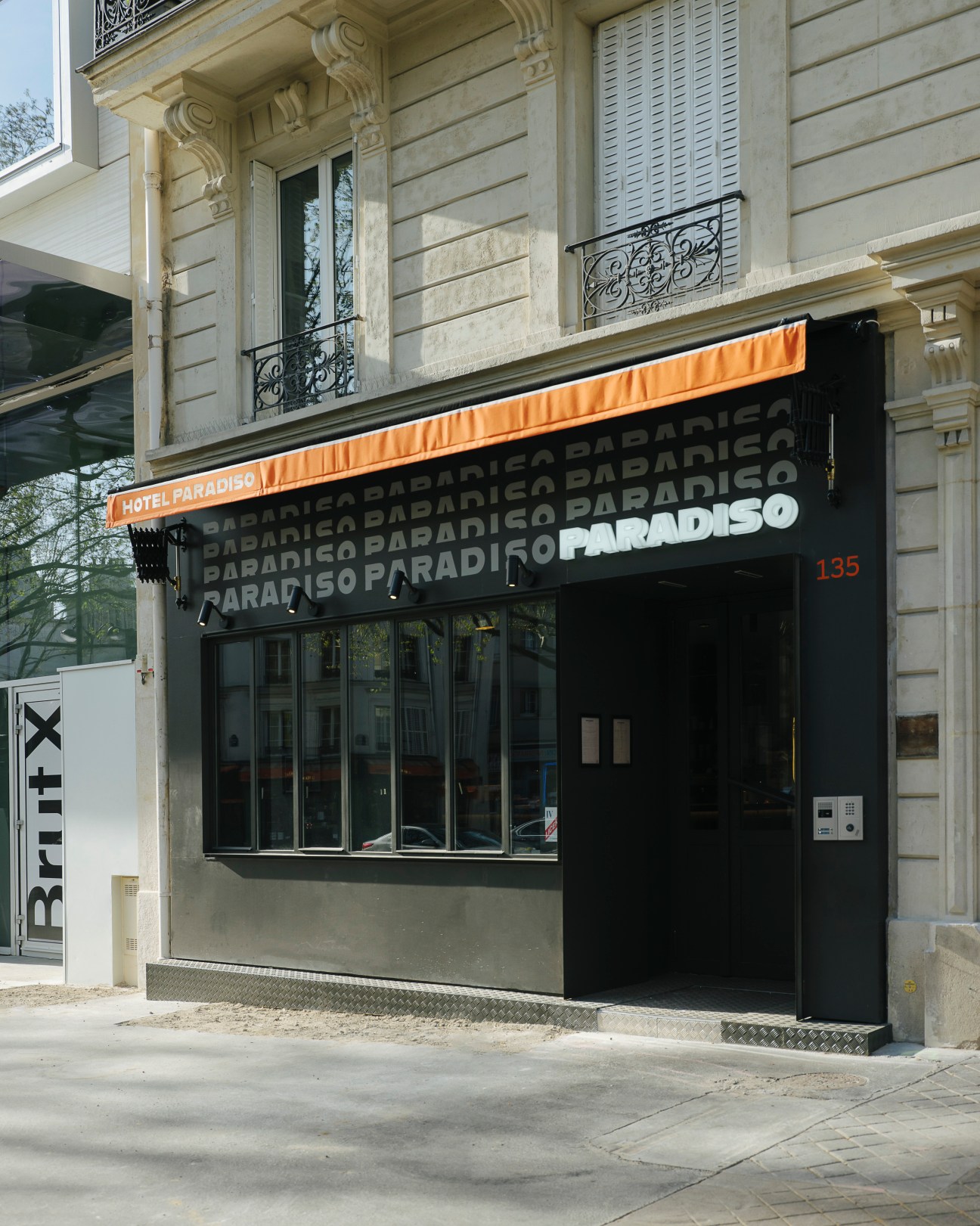 Street view of Hotel Paradiso with black storefront and orange awning on a Parisian building.