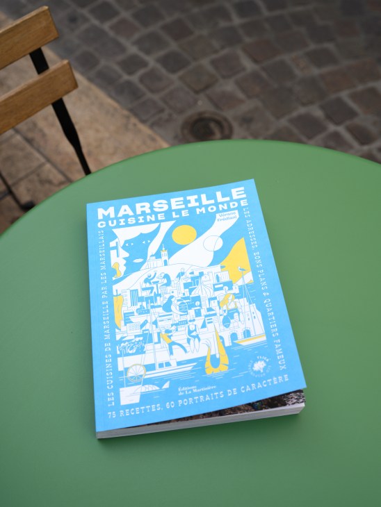 Marseille Cuisine le Monde cookbook on a green table with wooden chair visible.