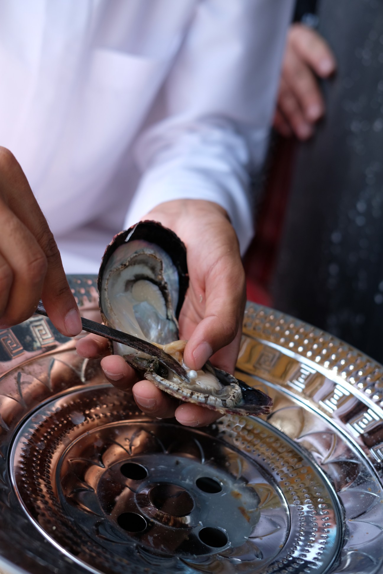A person holding an open oyster shell over decorative copper plates.