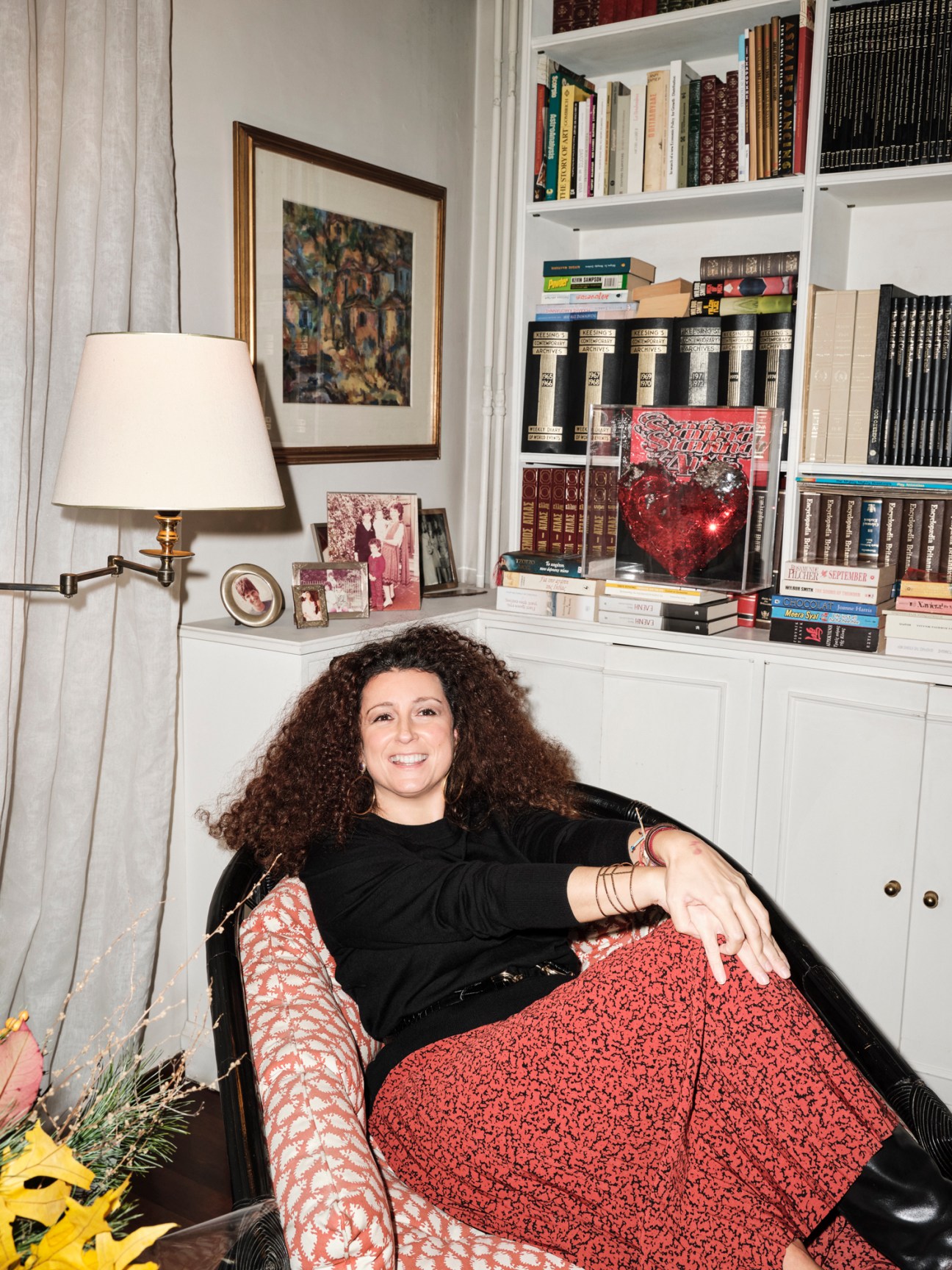 Katerina Vrana sits in a black leather chair in a home library with built-in bookshelves