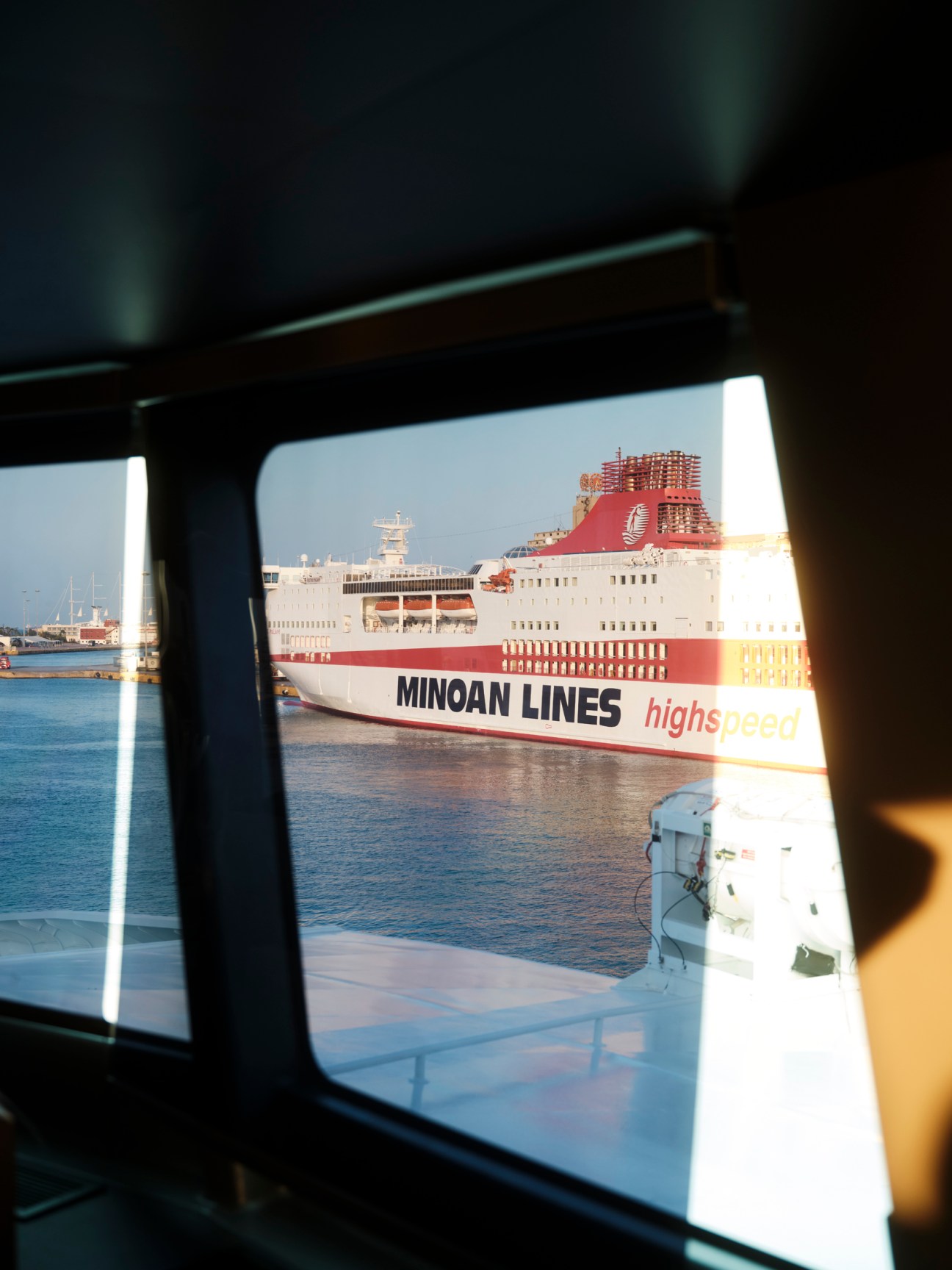 View from ferry window showing a Minoan Lines high-speed ferry docked at a Greek port in bright sunlight