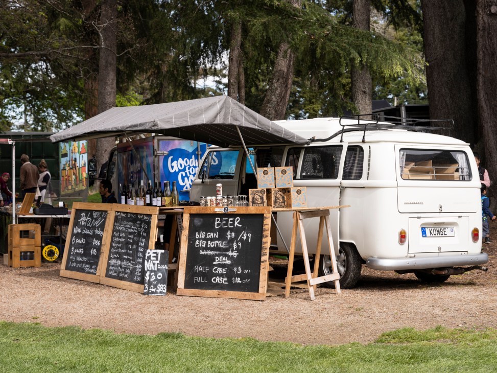 A white Volkswagen van converted into a mobile food and drink vendor with chalkboard menus and beer prices displayed