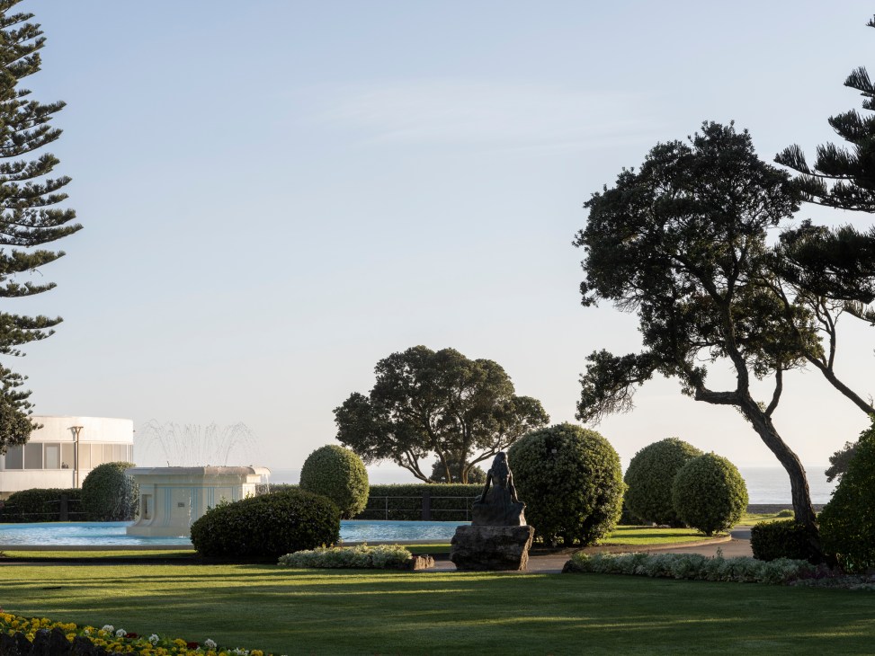 A manicured park with swimming pool, fountains, and mature trees overlooking water