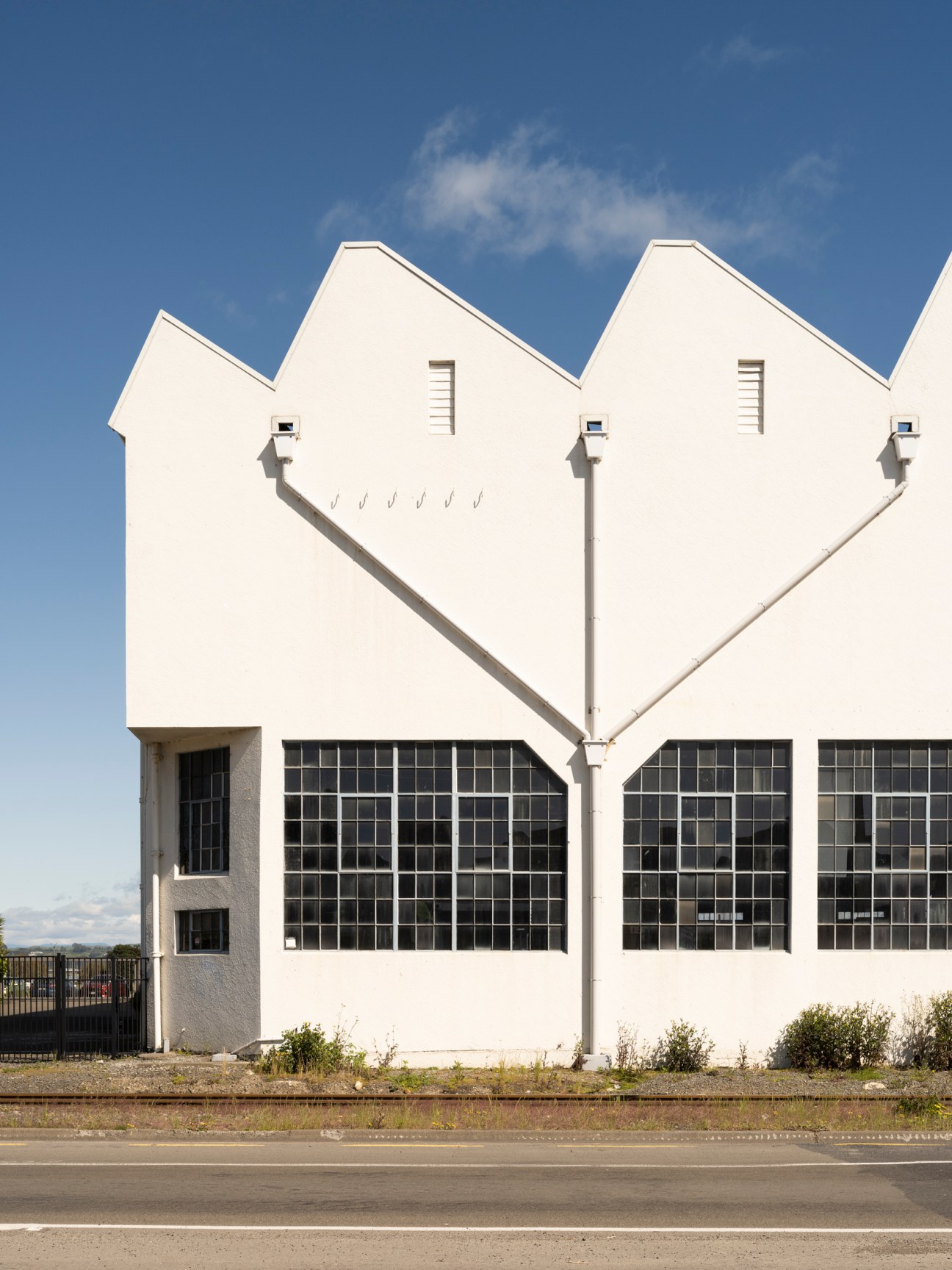 White industrial building with distinctive angular roof featuring triangular sections and large grid windows