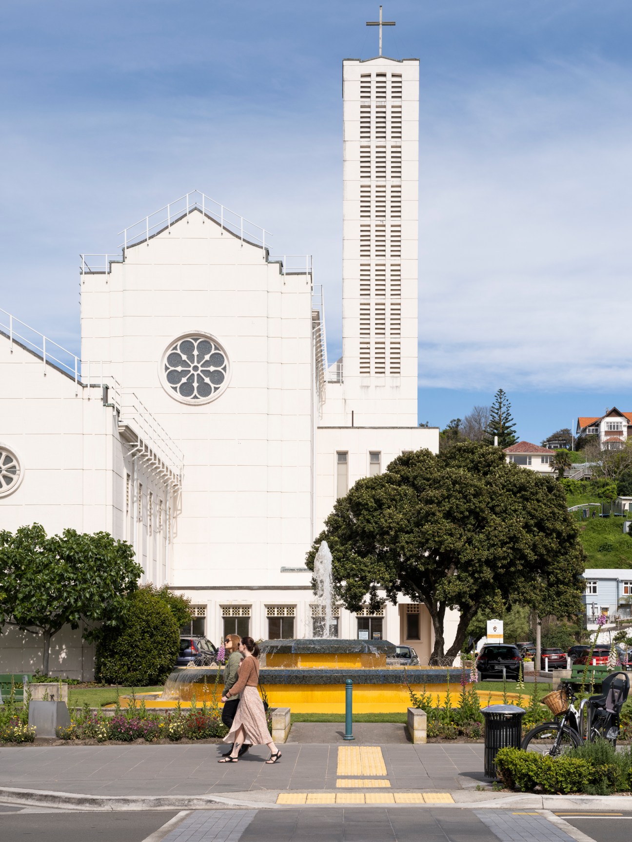 Modern white church building with tall bell tower and cross, featuring Art Deco architecture with circular rose window