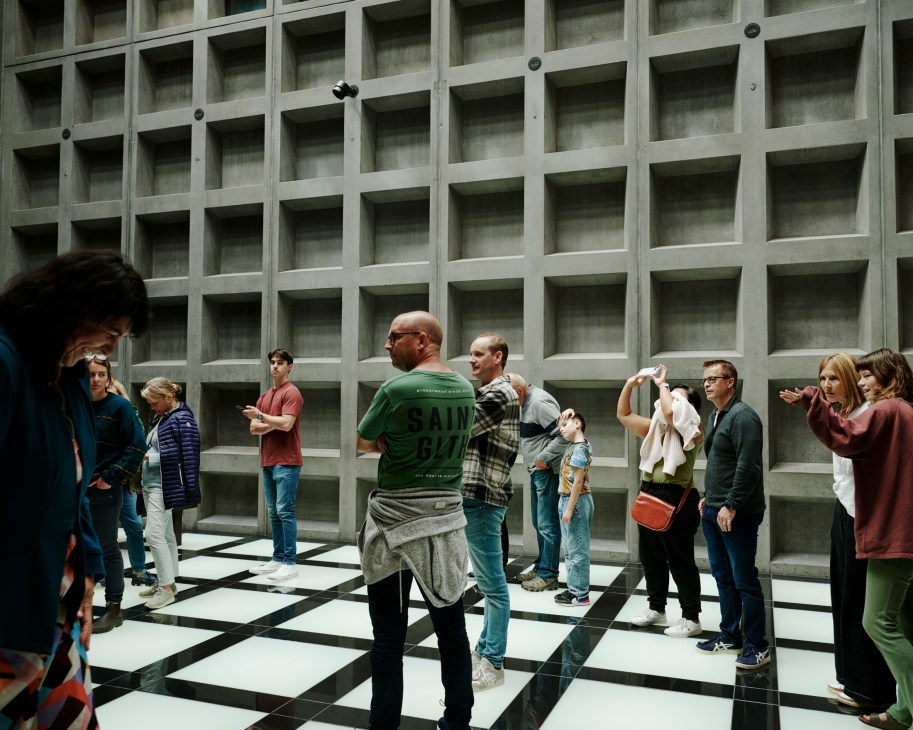 Visitors standing on checkered floor viewing concrete grid wall installation in museum gallery space