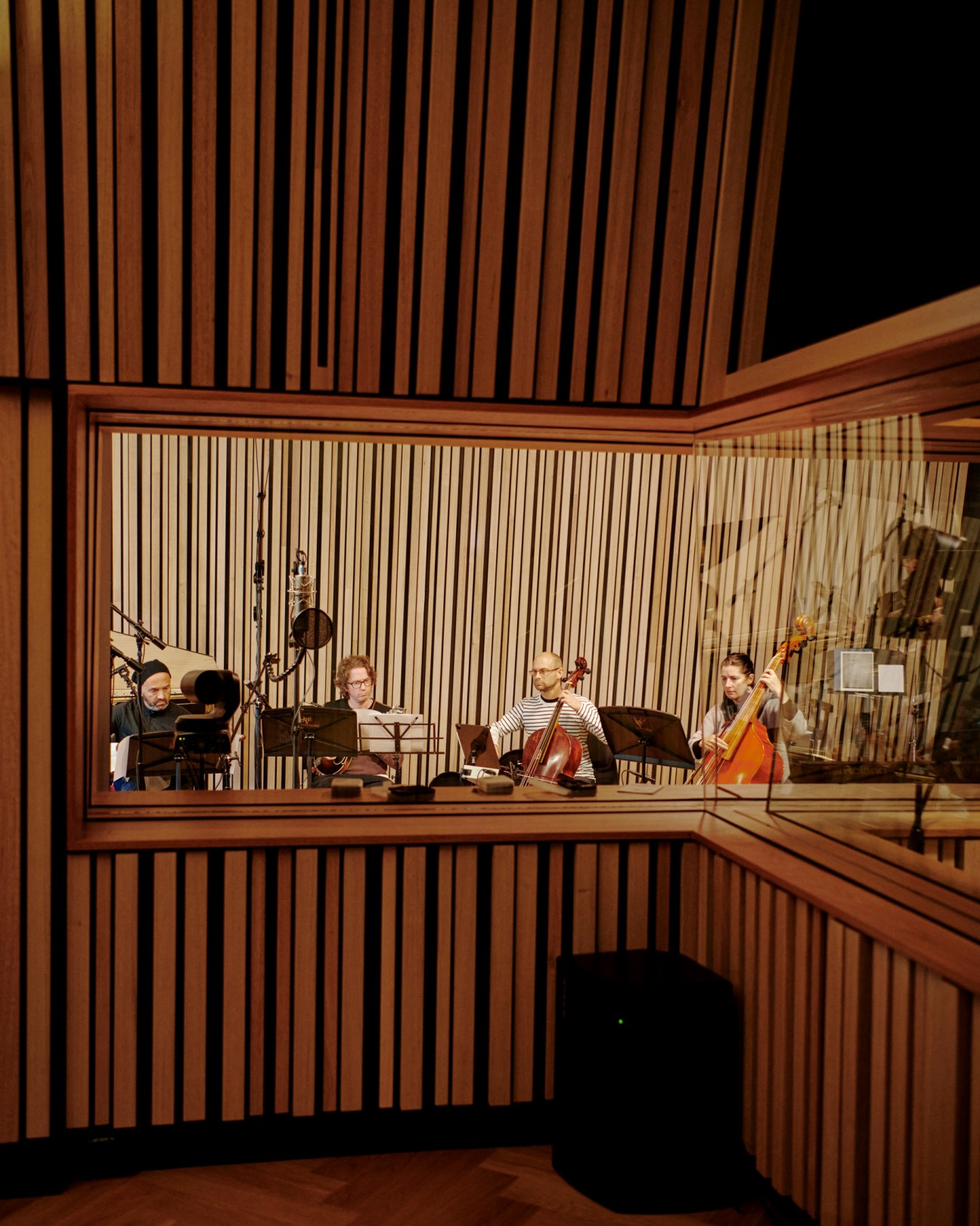 Musicians performing with string instruments in a modern recording studio viewed through glass panels