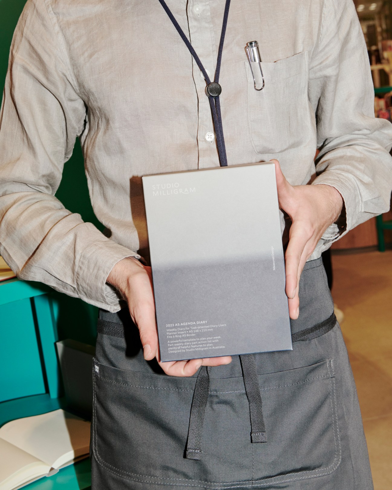 Person in beige shirt and apron holding Studio Milligram branded diary with both hands