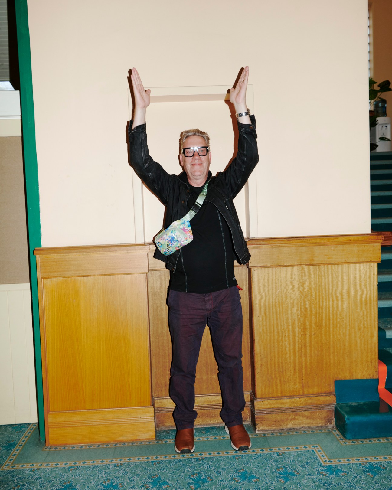 Brian Ritchie stands with arms raised in celebration, wearing glasses and a black leather jacket