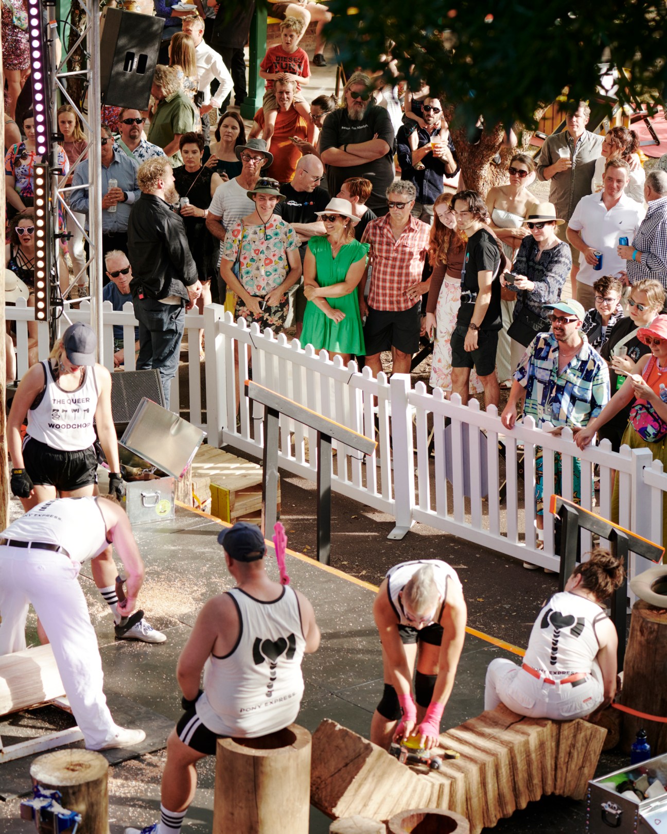 Performance artists chopping wood blocks while crowd watches behind white fence at outdoor festival event