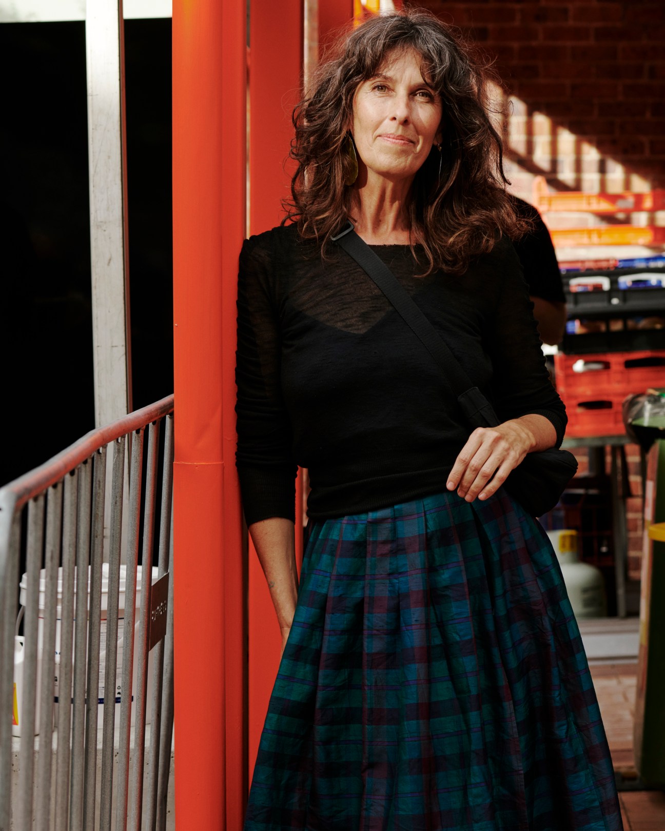 Woman in black top and plaid skirt standing by metal railing in colorful interior space