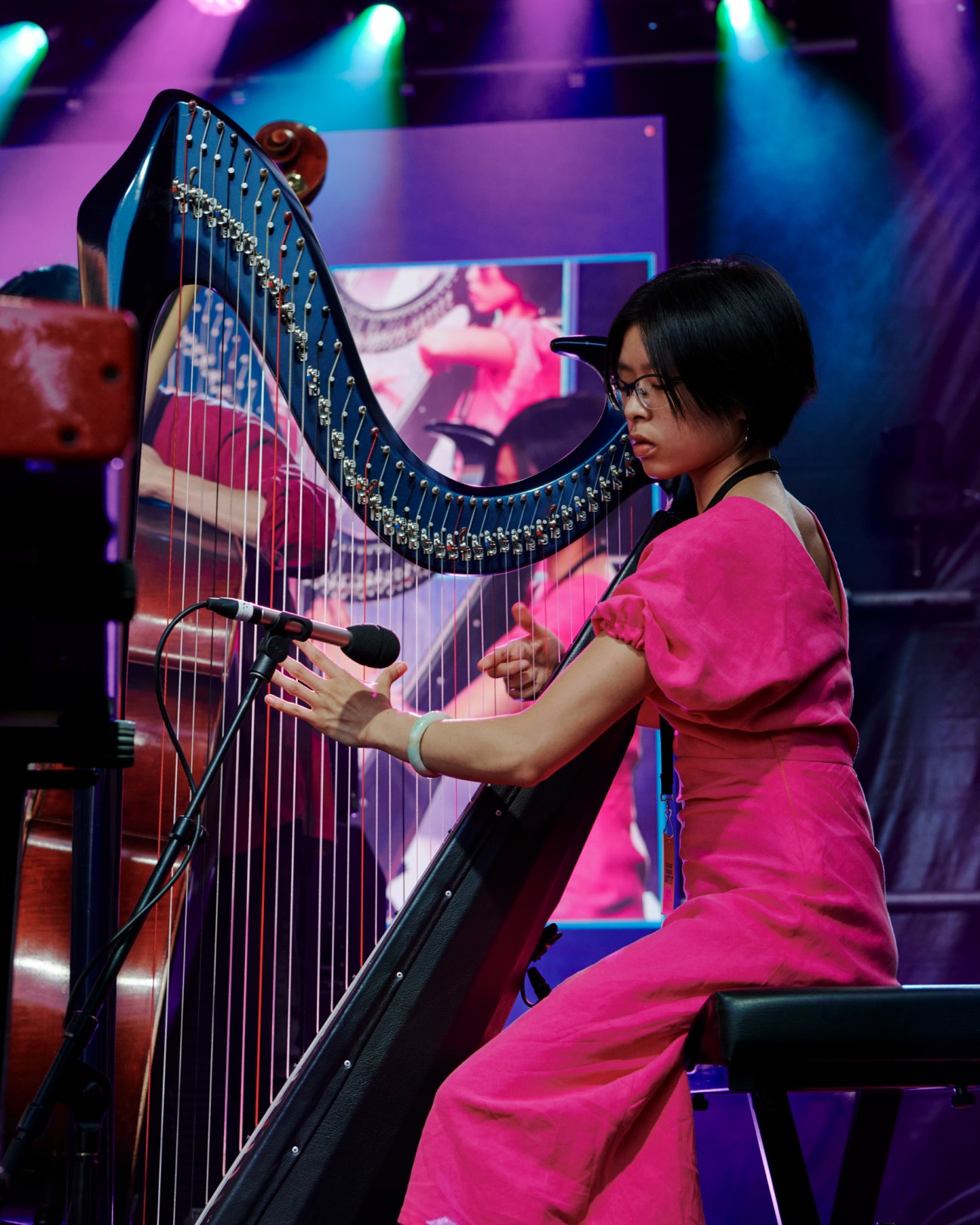 Harpist performing on stage at the Alice Coltrane tribute concert with colorful stage lighting
