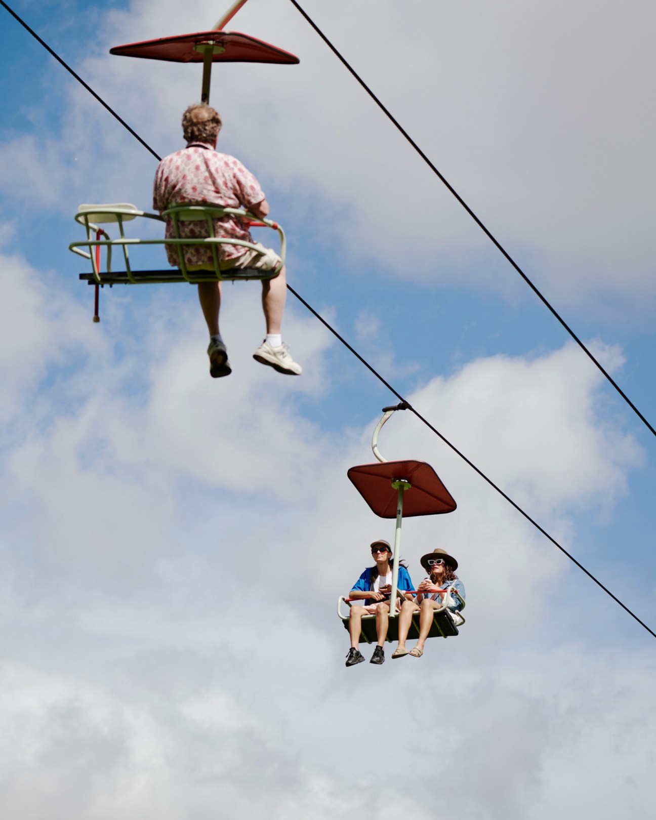 People riding on chairlift gondolas with red umbrellas against cloudy sky
