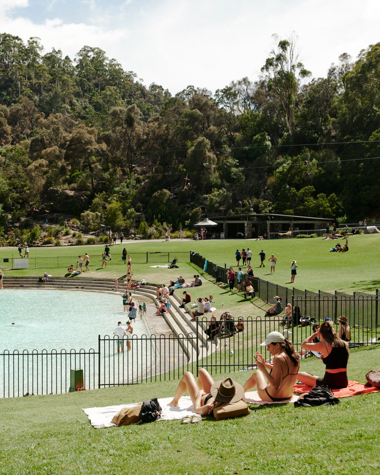 People sunbathing on grass near a swimming pool with steps leading into the water at Cataract Gorge