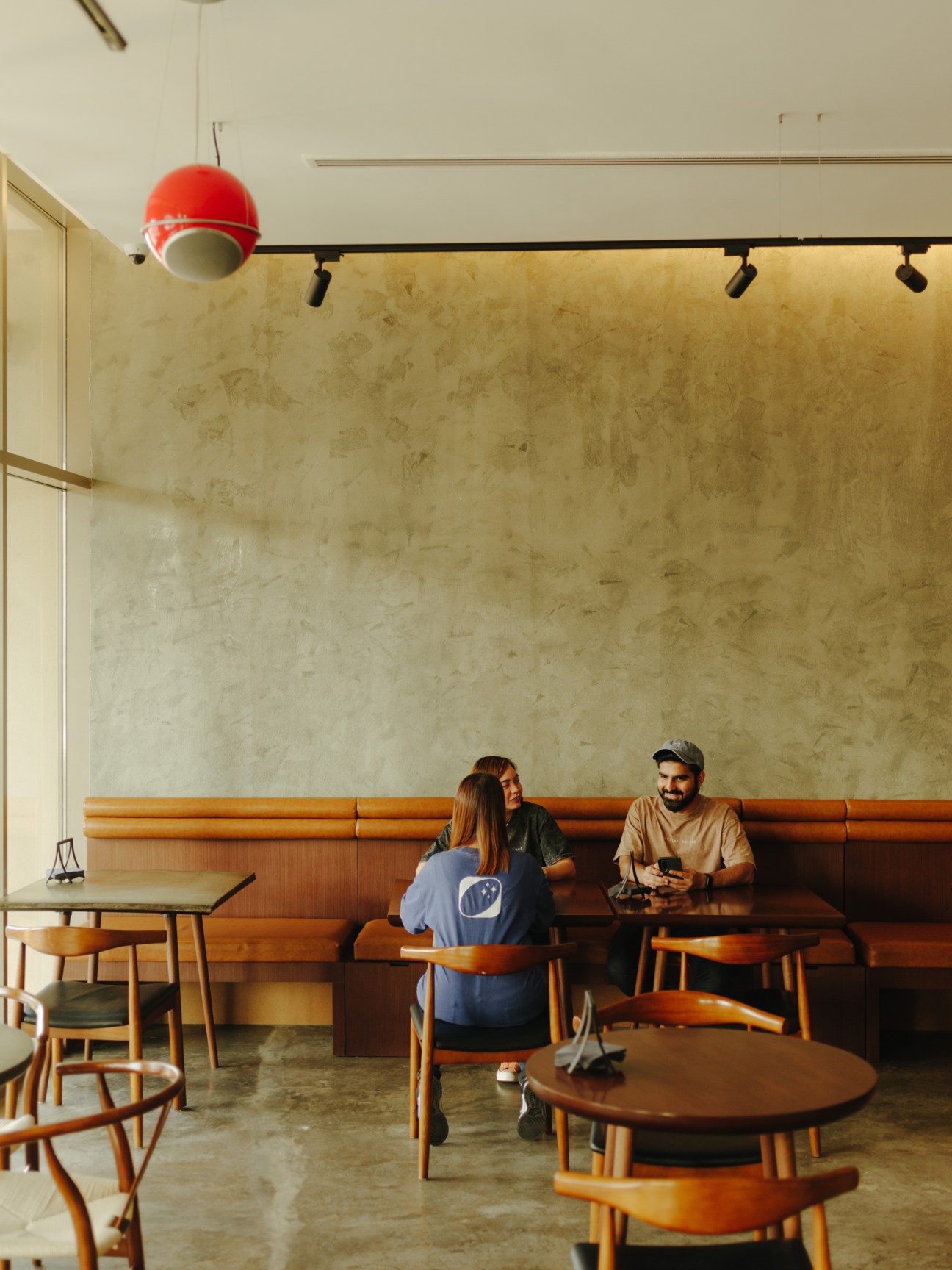 Interior of a modern coffee shop with customers seated at wooden tables and a red pendant light.