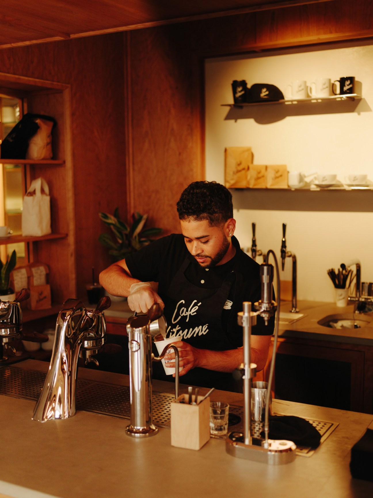 Barista in black shirt pouring coffee at modern espresso machine with metal taps and shelving in background