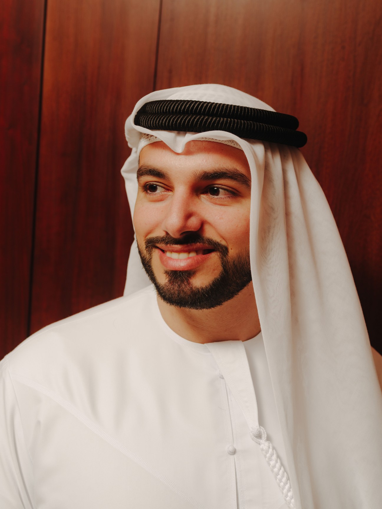 Portrait of DCDE vice president Saeed Al Gergawi wearing traditional Emirati white dishdasha and black ghutra against a red background.