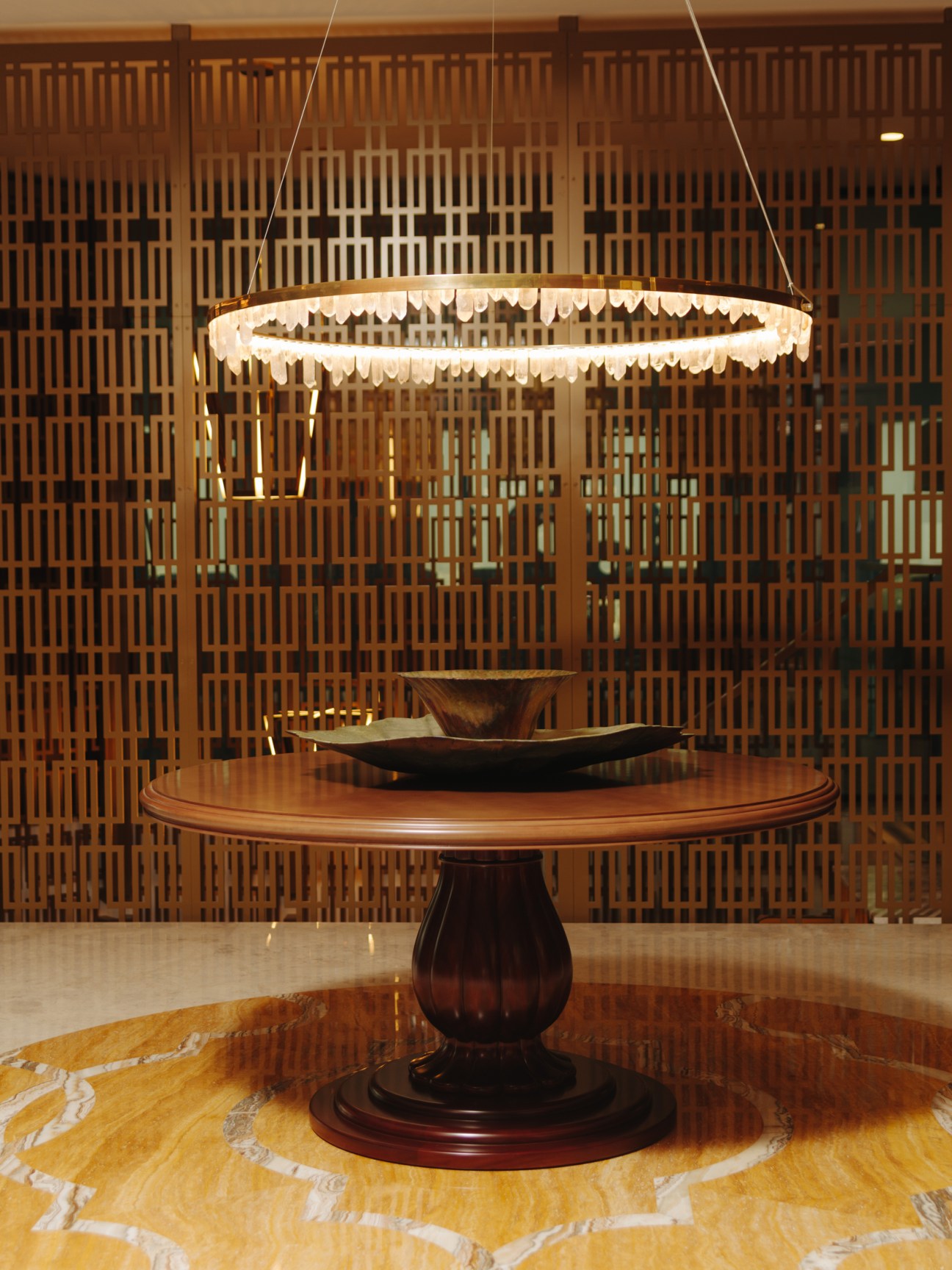 Interior of Dubai Chamber building with round wooden table under decorative pendant light and wooden lattice wall backdrop.