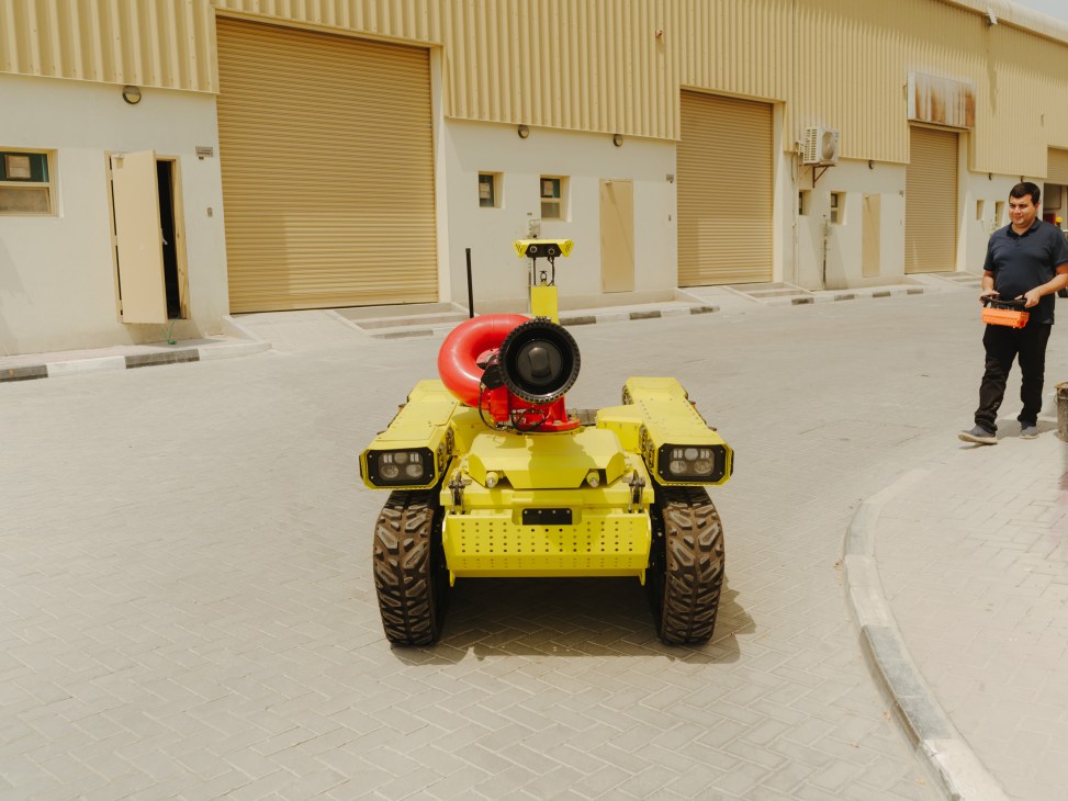 Mohammed Islam operates a yellow tracked robot with a red water cannon in a Dubai industrial courtyard.