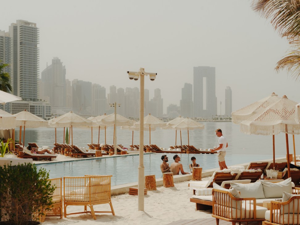 Kyma beach club on Palm Jumeirah with lounge chairs, umbrellas, infinity pool and Dubai skyline in background.