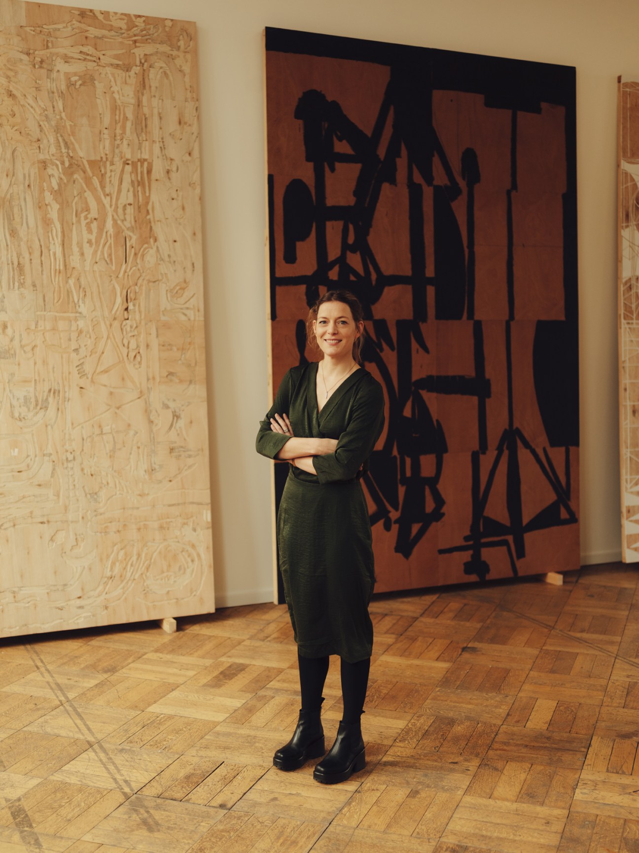 Woman in dark green dress standing with arms crossed in front of abstract artwork in gallery space