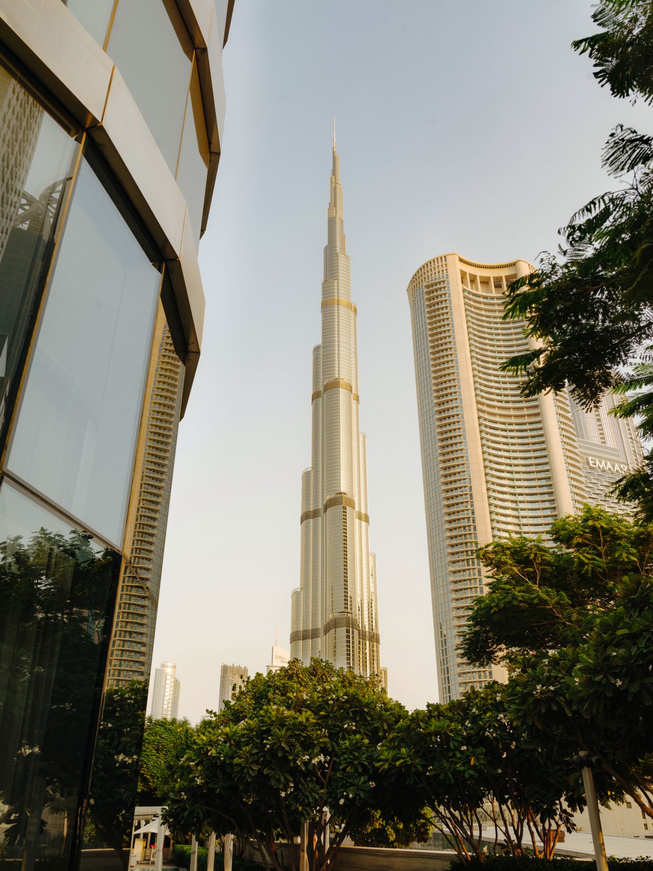Dubai skyline with Burj Khalifa tower and modern high-rise buildings surrounded by green vegetation.