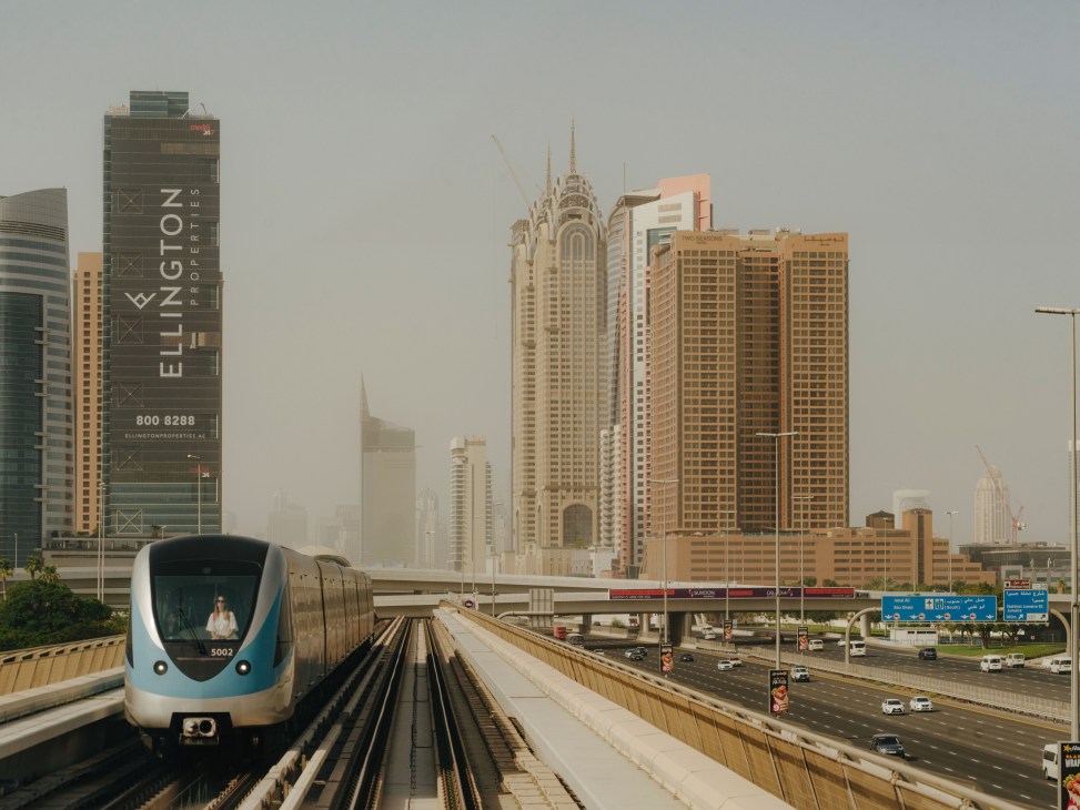 Dubai metro train on elevated tracks with city skyline and highway in background.