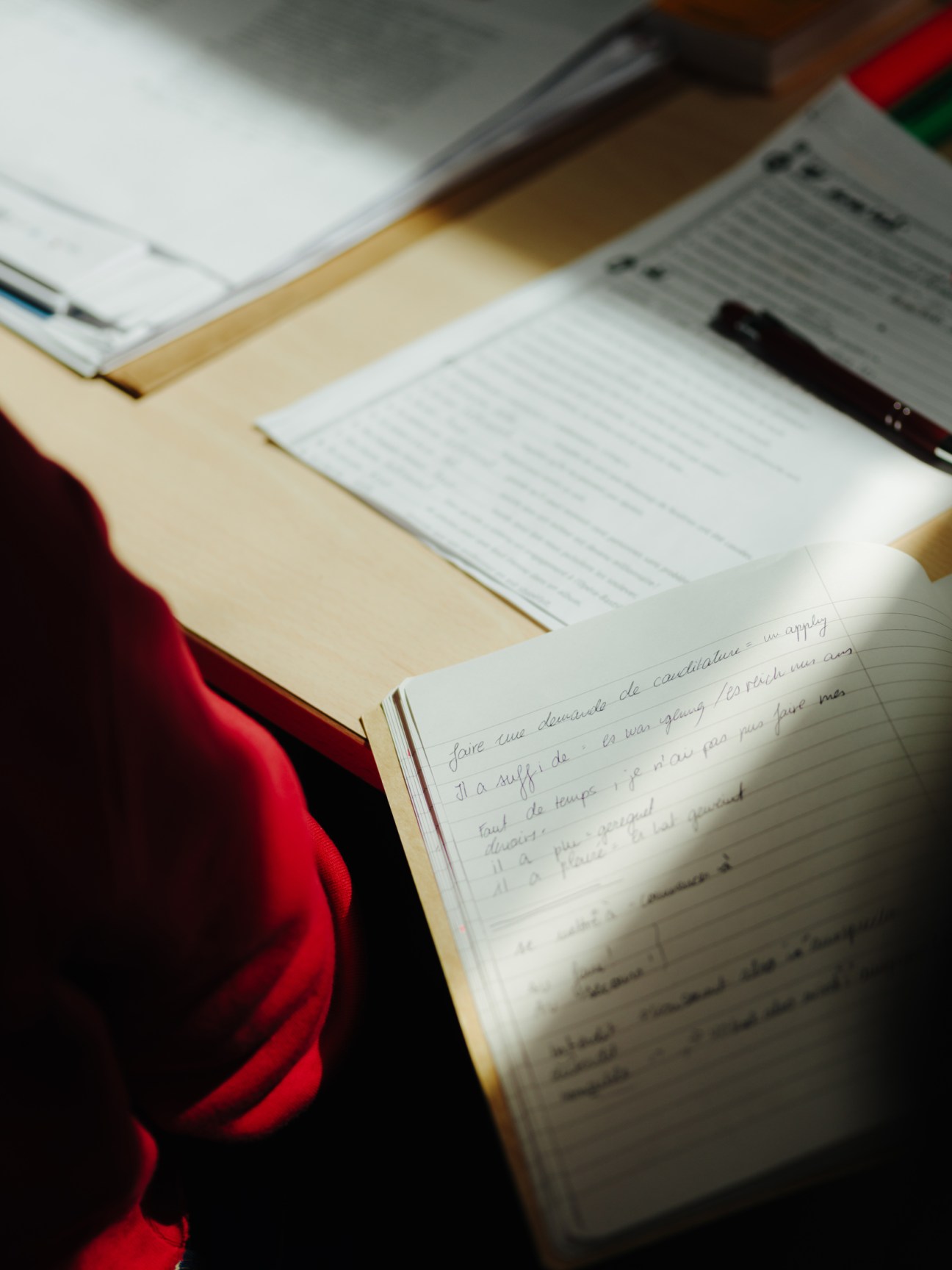 Student writing handwritten notes in French in a lined notebook during language class