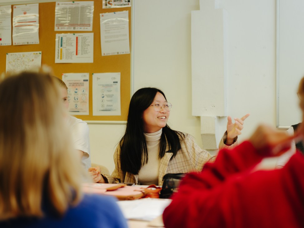 Students practicing French vocabulary in a classroom with a teacher pointing to materials on a wall