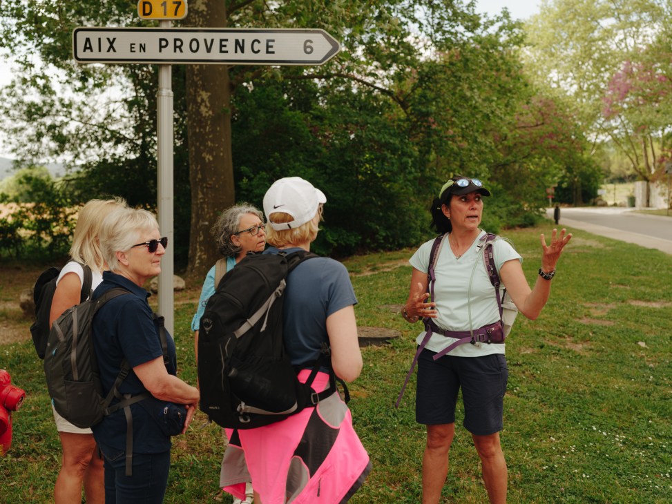 Tour guide gesturing while speaking to group of language students outdoors near road sign