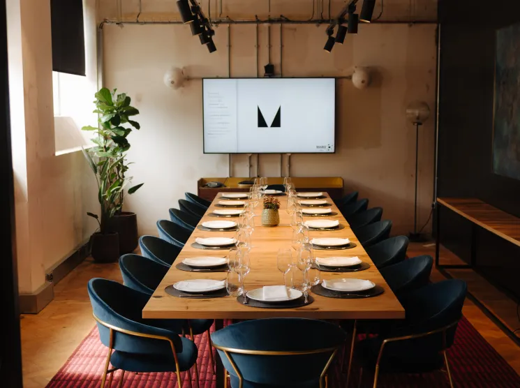 The Ministry workspace dining room with long wooden table, navy velvet chairs, and central bar in London.