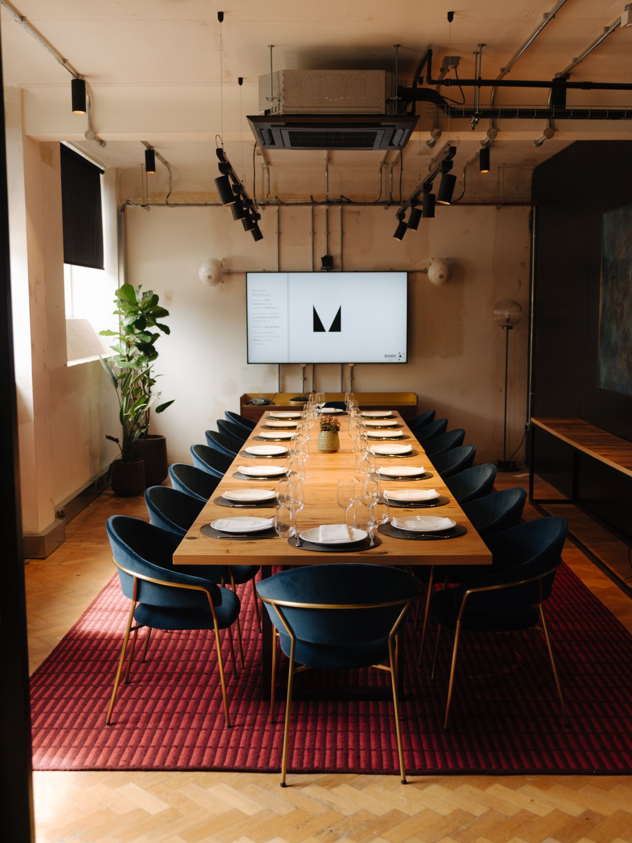 The Ministry workspace dining room with long wooden table, navy velvet chairs, and central bar in London.